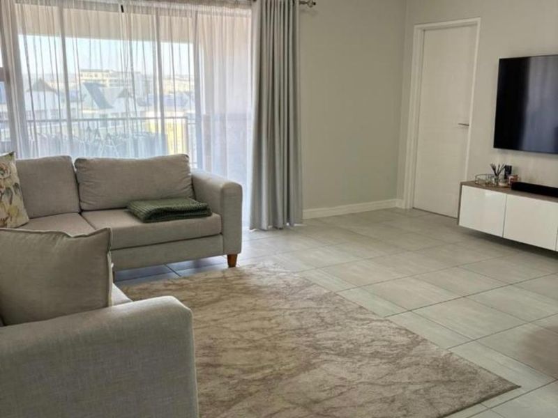 A bright and well-maintained living room featuring neutral tiled flooring, large sliding glass doors with curtains, and clean finishes throughout.