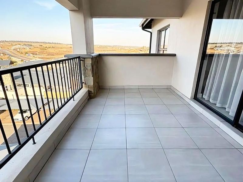 A spacious covered balcony featuring modern tiled flooring, a metal balustrade, and expansive views of the surrounding landscape.