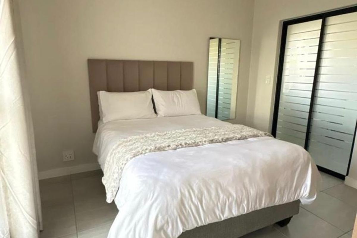 A well-maintained bedroom featuring neutral tiled flooring, a modern pendant light, and a sliding glass door providing natural light.