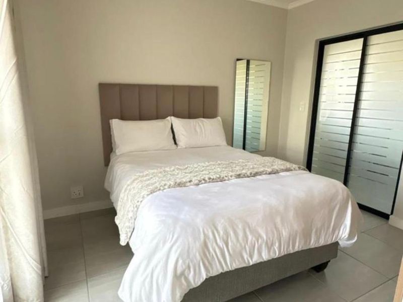 A well-maintained bedroom featuring neutral tiled flooring, a modern pendant light, and a sliding glass door providing natural light.