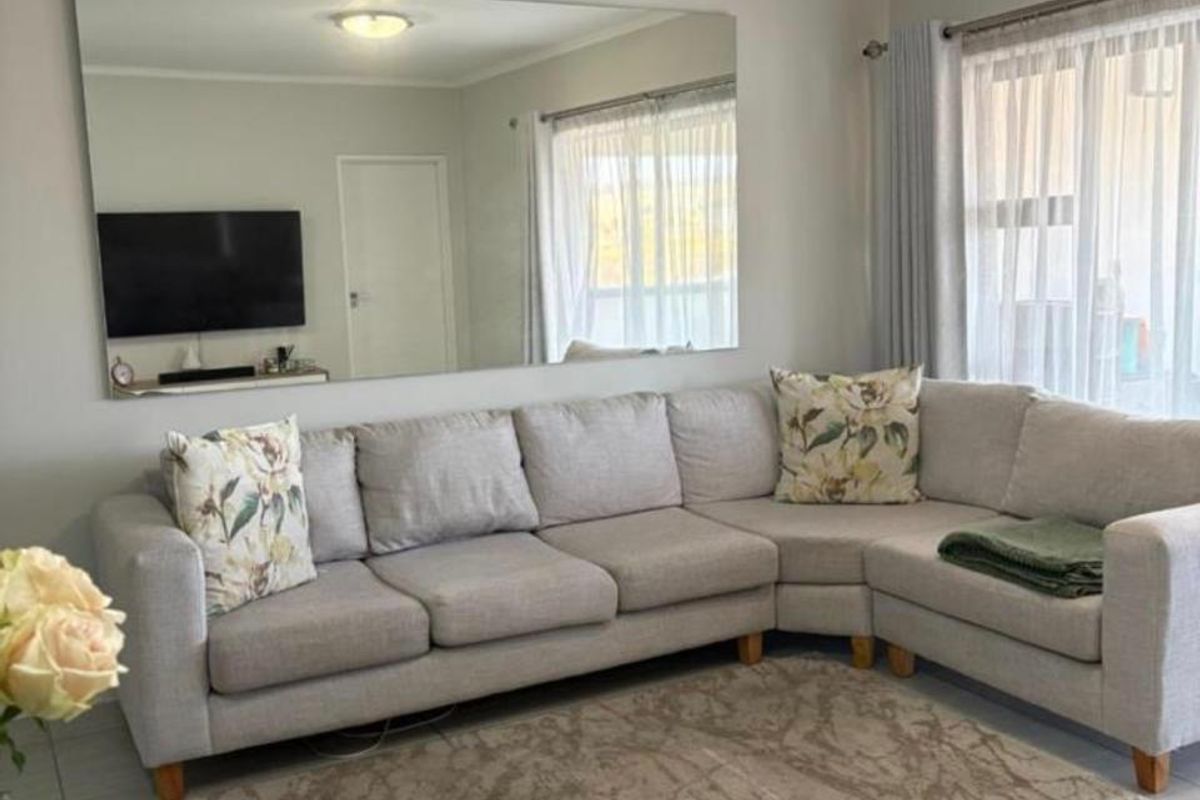A bright and well-maintained living room featuring neutral tiled flooring, a large wall-mounted mirror, and ample natural light through window treatments.
