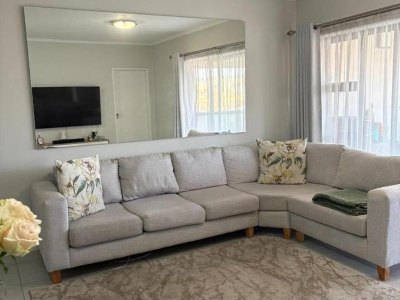 A bright and well-maintained living room featuring neutral tiled flooring, a large wall-mounted mirror, and ample natural light through window treatments.