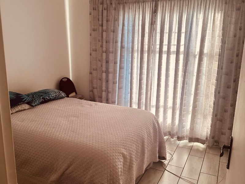 A bedroom featuring tiled flooring and large window curtains, providing a functional and well-lit space.