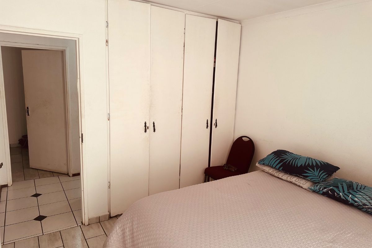 A bedroom featuring built-in cupboards and tiled flooring, offering a functional space with potential for cosmetic updates.