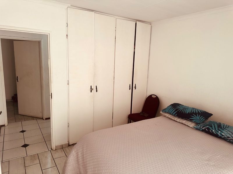 A bedroom featuring built-in cupboards and tiled flooring, offering a functional space with potential for cosmetic updates.