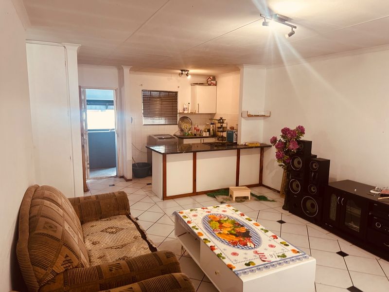 Open-plan living and kitchen area featuring tiled flooring, a central kitchen island with a built-in hob, and direct access to an outdoor balcony.