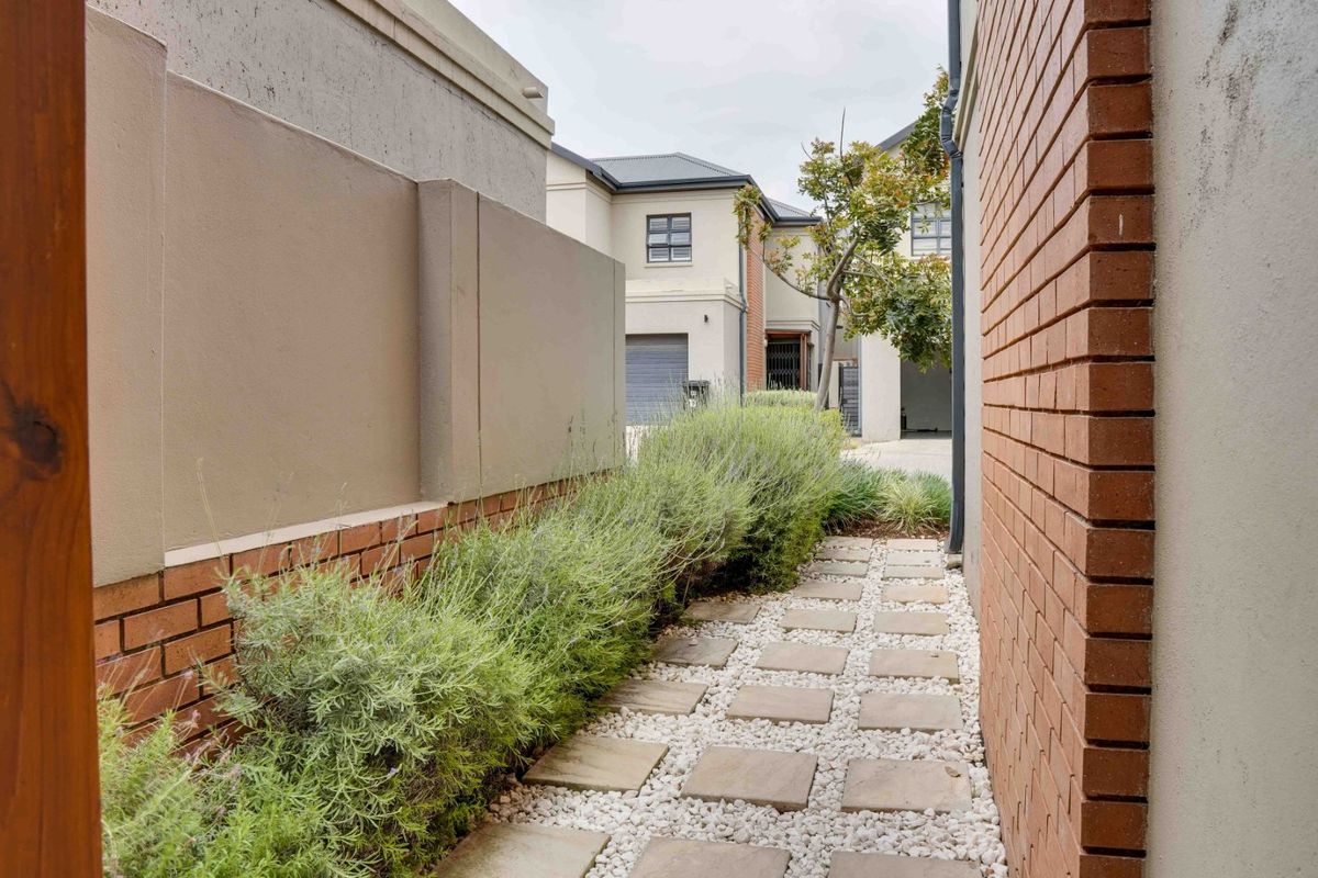 A well-maintained side walkway featuring a stone paver path, gravel landscaping, and brick boundary walls within a townhouse complex.