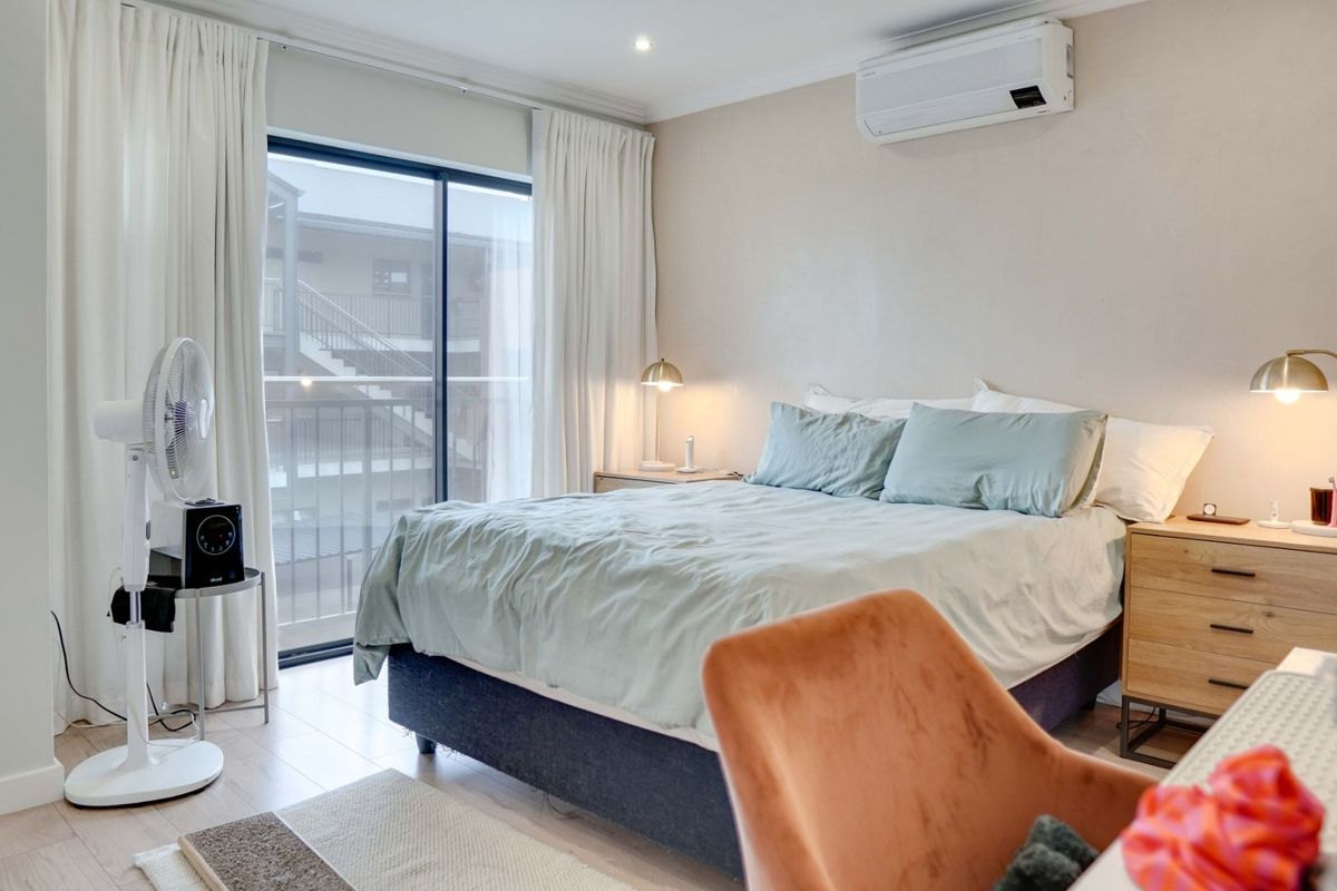 A well-maintained bedroom featuring laminate flooring, a split-system air conditioner, and a sliding glass door providing access to an outdoor balcony area.