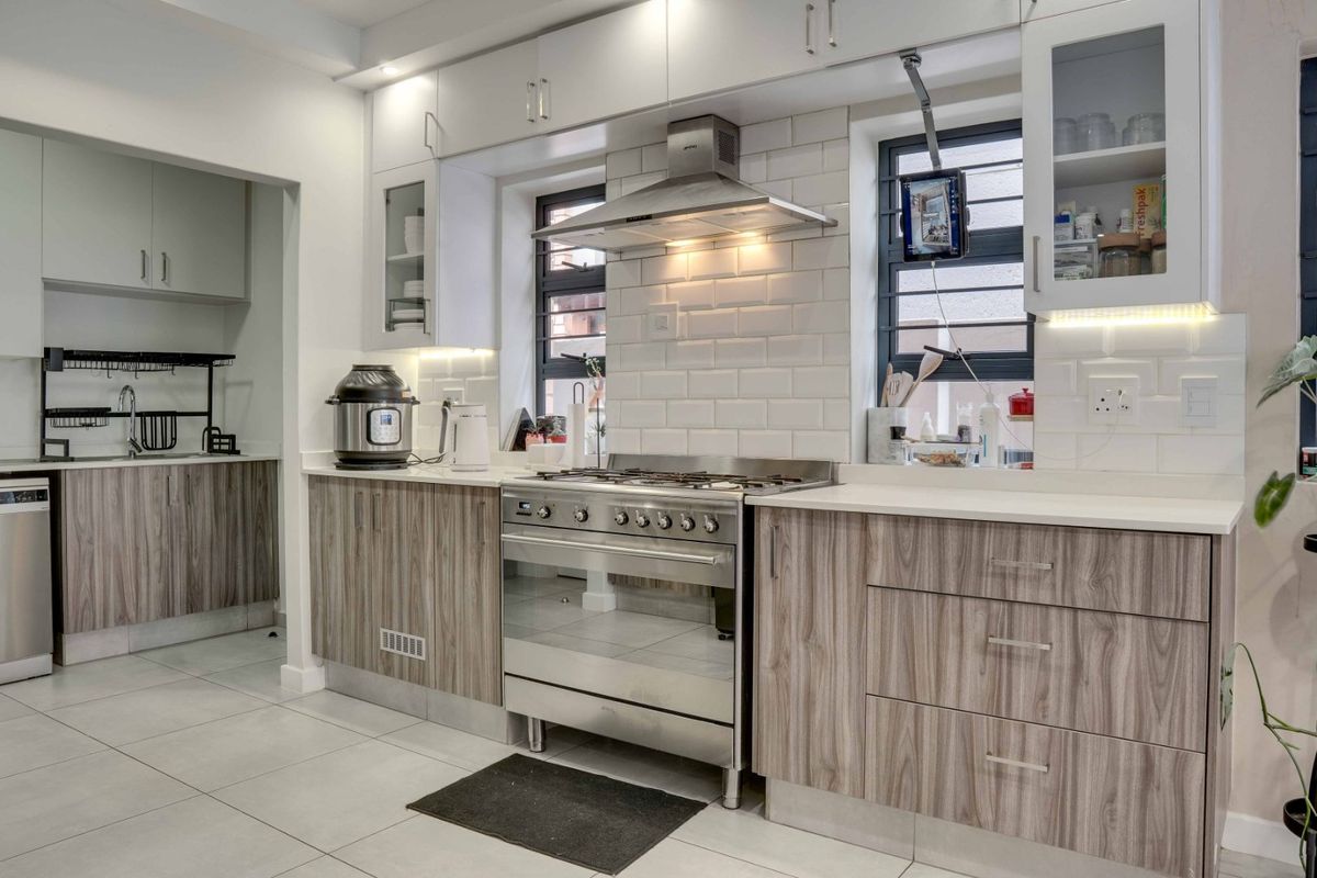 Modern kitchen featuring wood-grain cabinetry, stone countertops, subway tile backsplash, and a stainless steel gas stove with an integrated extractor fan.