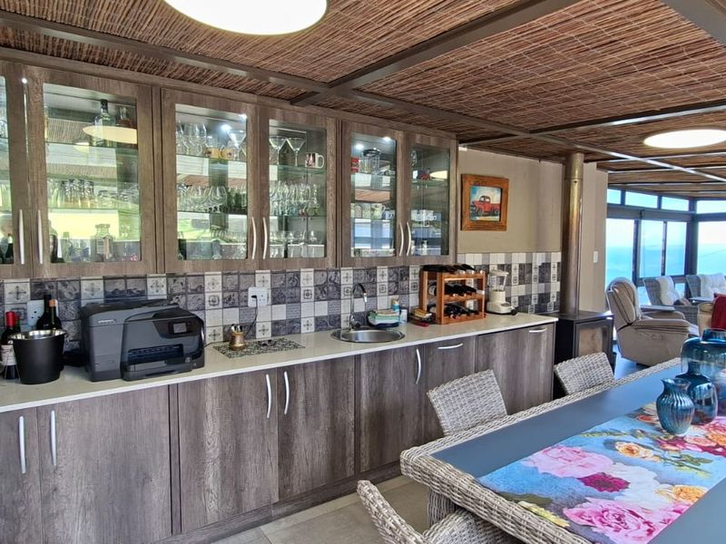 Spacious open-plan living and dining area featuring a modern built-in bar or kitchenette with glass-fronted cabinetry, tiled backsplash, and a cozy fireplace.