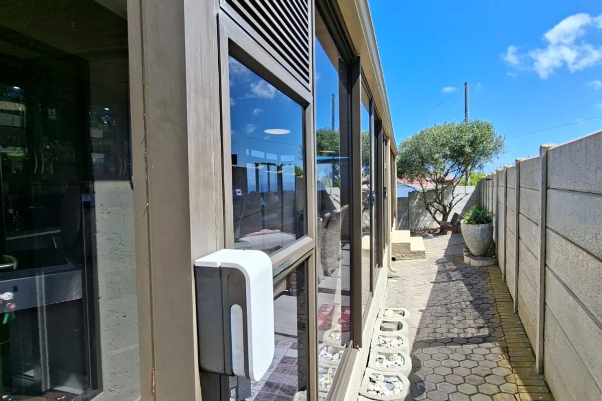 A side exterior view showing a paved walkway alongside the house, featuring a precast concrete boundary wall and aluminium sliding door access.
