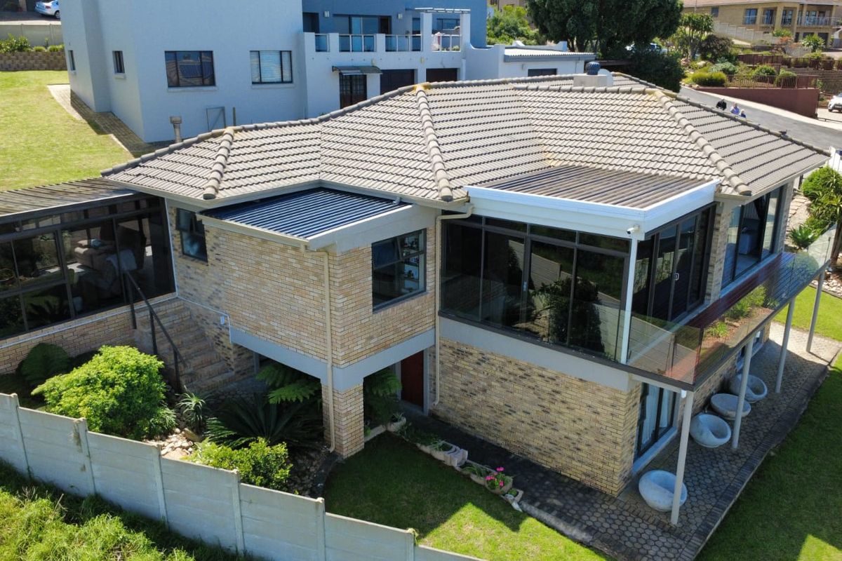 Aerial view of a multi-level brick house featuring a tiled roof, glass balustrades, and a covered patio area set within a landscaped garden.
