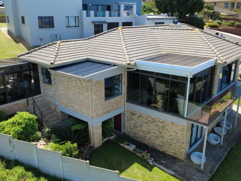 Aerial view of a multi-level brick house featuring a tiled roof, glass balustrades, and a covered patio area set within a landscaped garden.