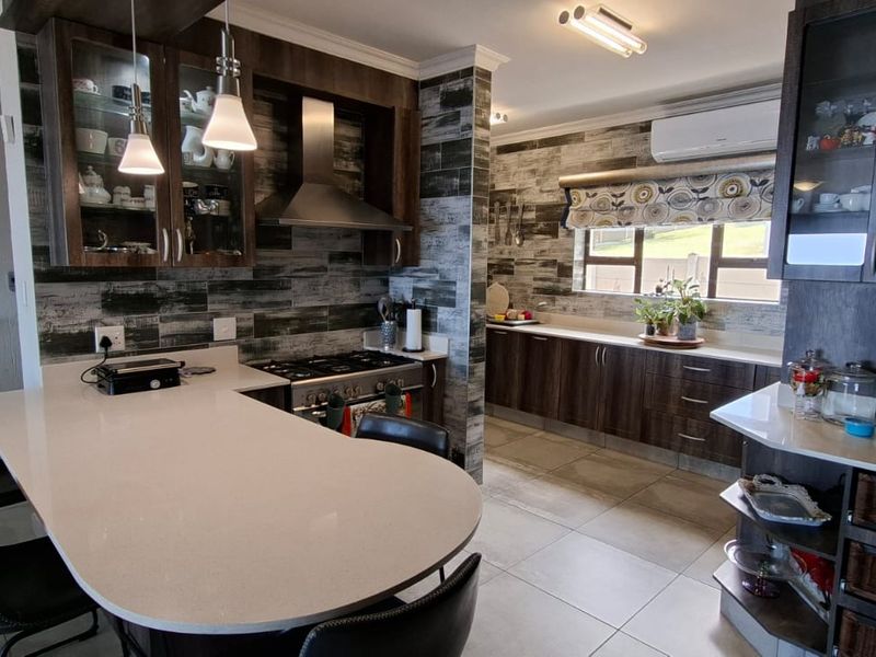 Modern kitchen featuring dark wood cabinetry, quartz countertops, a gas hob with extractor, and tiled flooring, offering a functional and stylish cooking space.