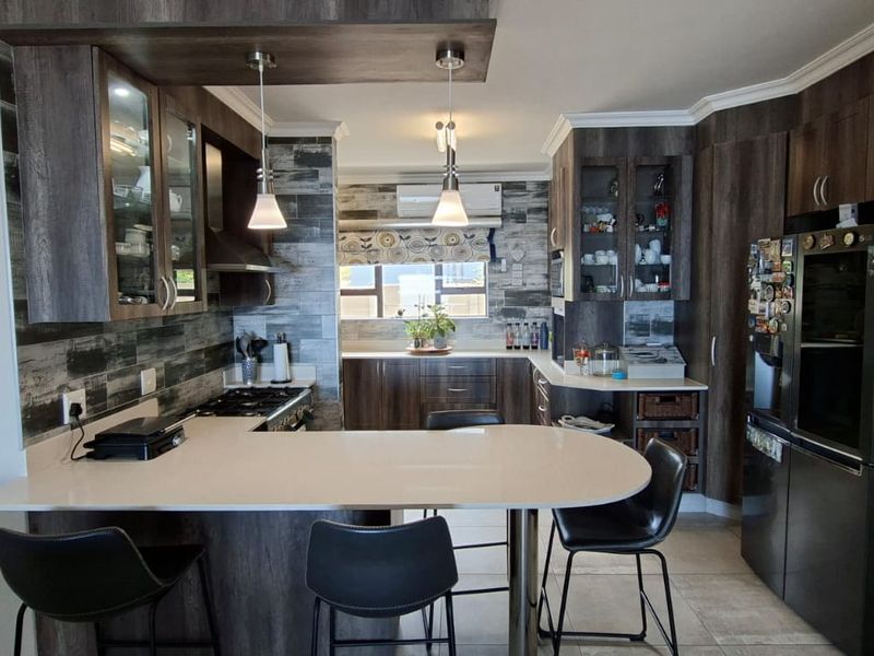 Modern kitchen featuring dark wood cabinetry, stone countertops, a breakfast bar, integrated appliances, and stylish pendant lighting.