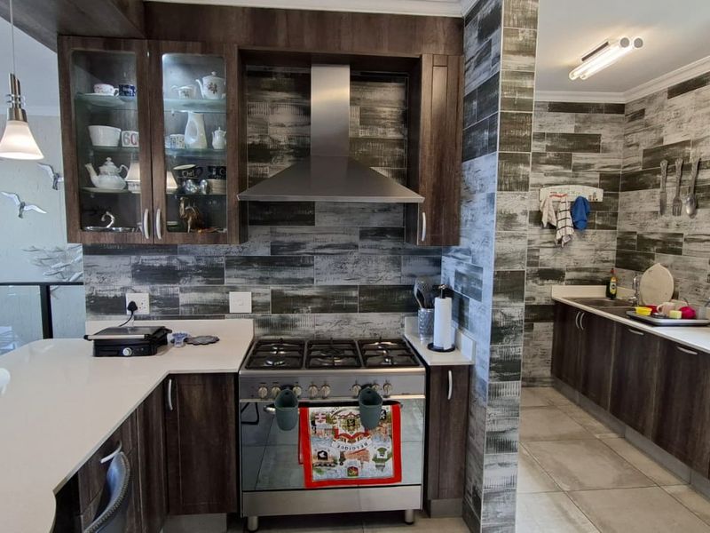Modern kitchen featuring dark wood cabinetry, stone countertops, a gas stove with stainless steel extractor, and a separate scullery area with tiled finishes.