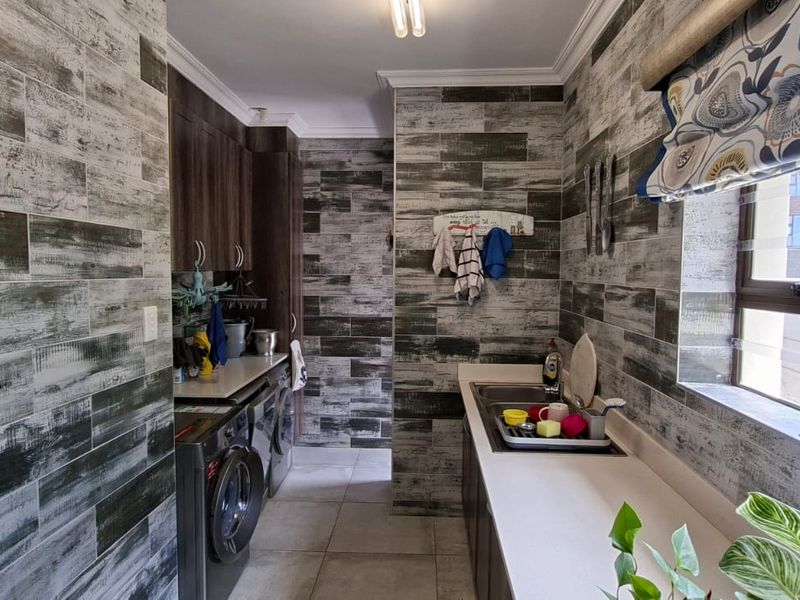 A functional scullery featuring extensive built-in cabinetry, tiled wall finishes, and a double basin sink with dedicated laundry appliance connections.