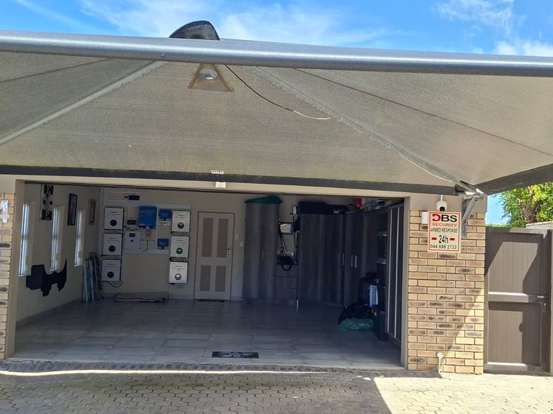 A well-maintained garage featuring tiled flooring, built-in cabinetry, and a solar inverter system, protected by an overhead shade sail.