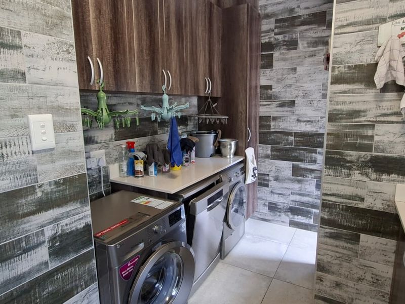 A functional laundry room featuring built-in cabinetry, laminate countertops, a stainless steel sink, and decorative wood-look tiled wall finishes.