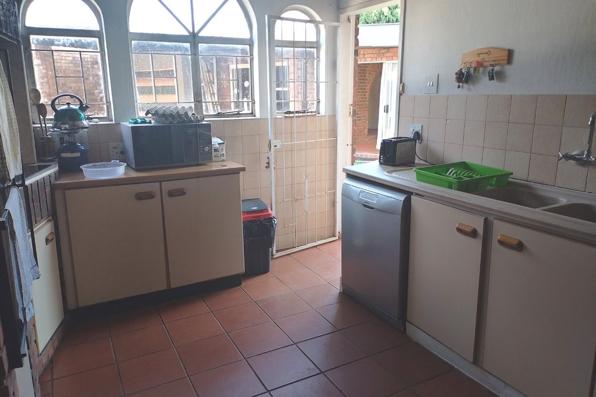 A functional kitchen featuring tiled flooring, built-in cabinetry, a double basin sink, and arched windows with direct access to the exterior.