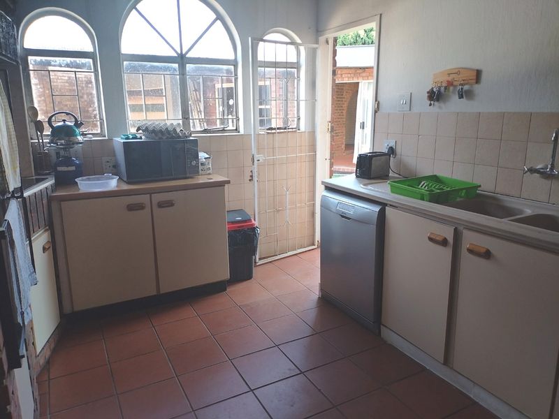 A functional kitchen featuring tiled flooring, built-in cabinetry, a double basin sink, and arched windows with direct access to the exterior.