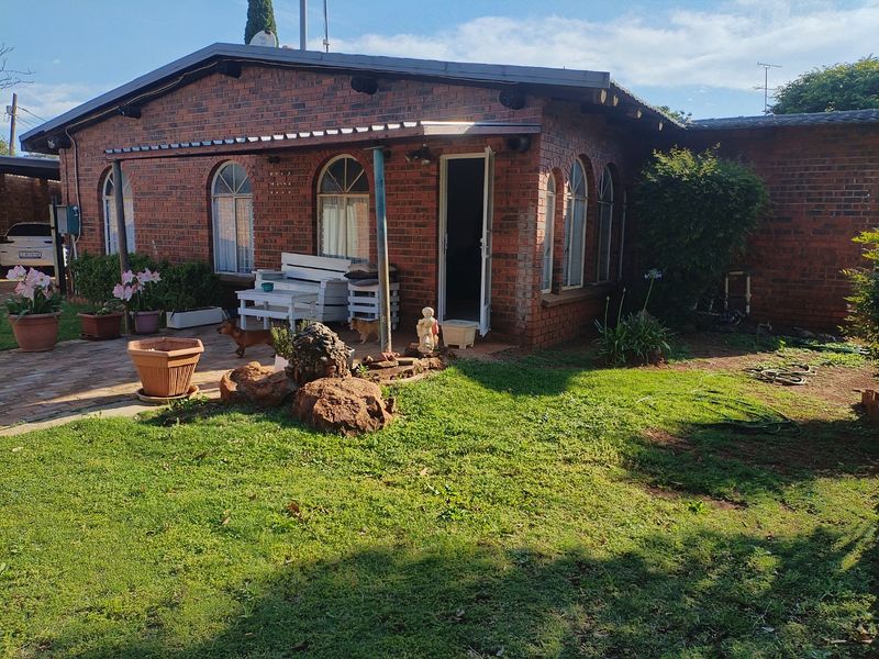 Rear view of a face brick house featuring arched windows and a paved patio area overlooking a garden.
