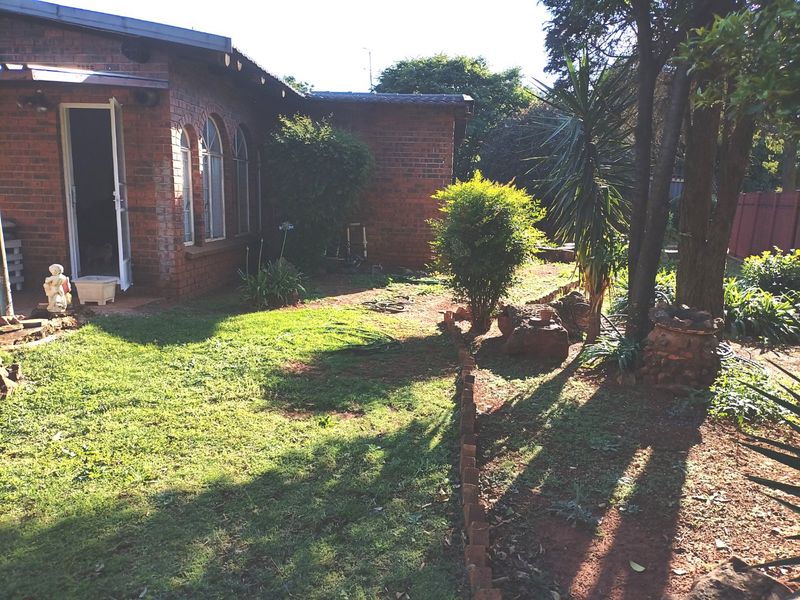 A rear garden view featuring a red brick house facade with arched windows and established trees.