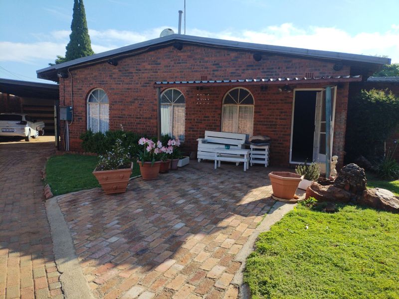Front view of a brick house featuring arched windows, a paved driveway, and a covered patio area.