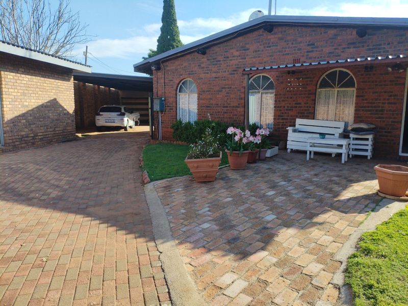 Front exterior view of a face brick house featuring arched windows, a paved driveway, and a covered carport area.