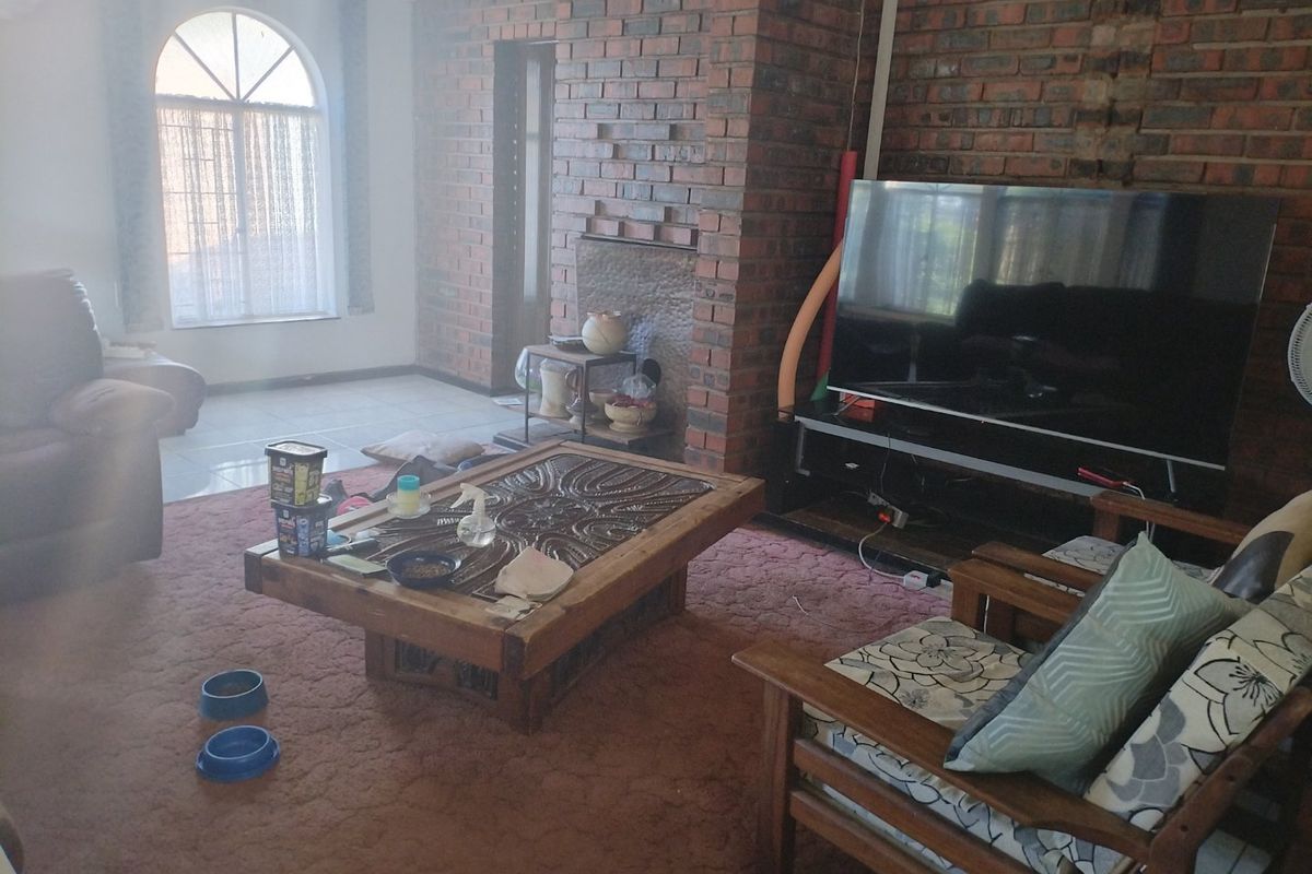 Living room featuring an exposed brick fireplace, arched window, and tiled flooring. The space requires cosmetic updates to improve its overall condition.