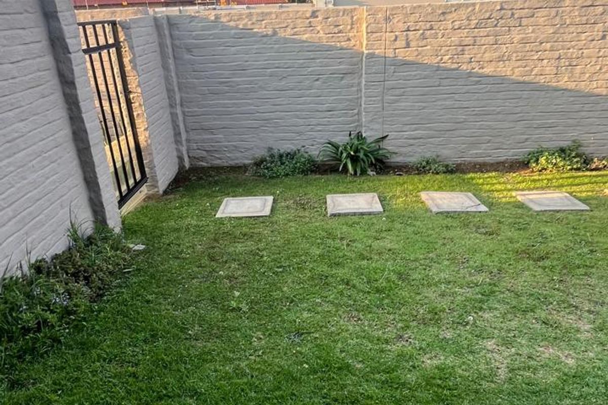 A private rear garden featuring a well-maintained lawn, concrete stepping stones, and a secure precast boundary wall with a metal pedestrian gate.