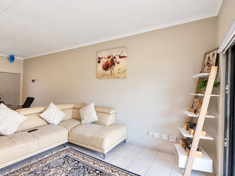 A bright and well-maintained living room featuring tiled flooring, neutral wall tones, and a large sliding glass door providing access to the outdoor area.