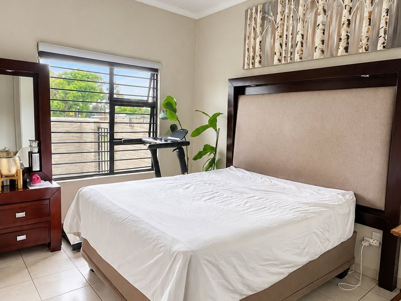 A well-maintained bedroom featuring neutral tiled flooring, a large window with security bars, and a clean, functional layout.