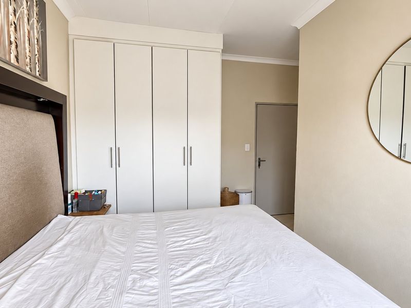 A well-maintained bedroom featuring neutral wall tones, built-in floor-to-ceiling cupboards, and clean architectural finishes.