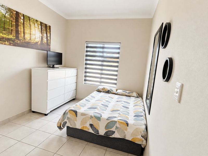 A well-maintained bedroom featuring neutral wall tones, tiled flooring, and modern roller blinds, providing a clean and functional living space.