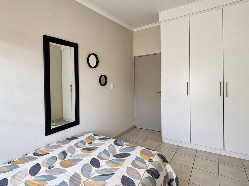 A well-maintained bedroom featuring neutral wall tones, practical built-in cupboards, and durable tiled flooring, offering a clean and functional living space.