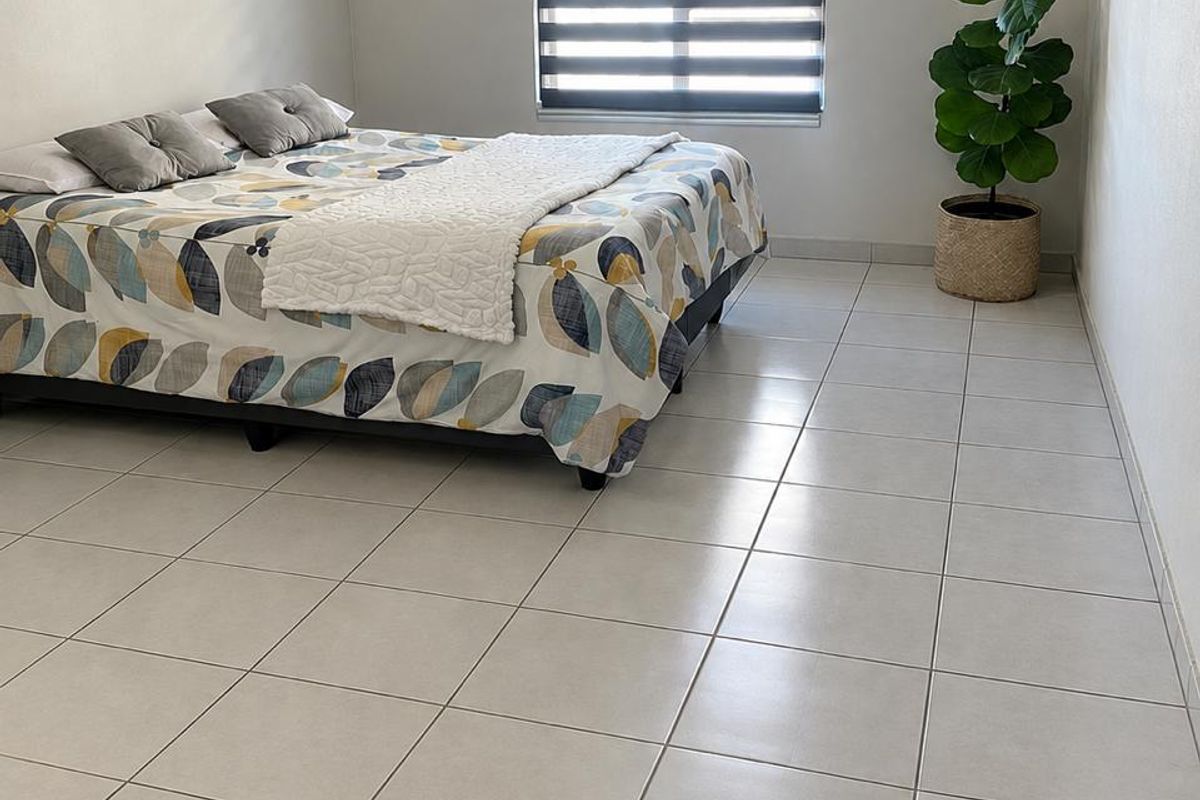 A clean and well-maintained bedroom featuring neutral tiled flooring and a modern dual-layer roller blind for adjustable natural light.