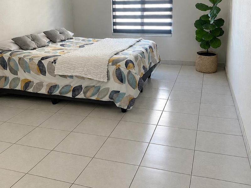 A clean and well-maintained bedroom featuring neutral tiled flooring and a modern dual-layer roller blind for adjustable natural light.