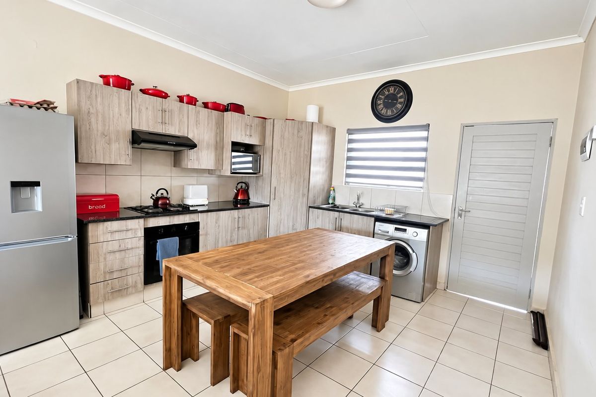 A functional kitchen featuring light wood-finish cabinetry, dark countertops, a gas hob, built-in oven, and tiled flooring with an integrated laundry appliance space.