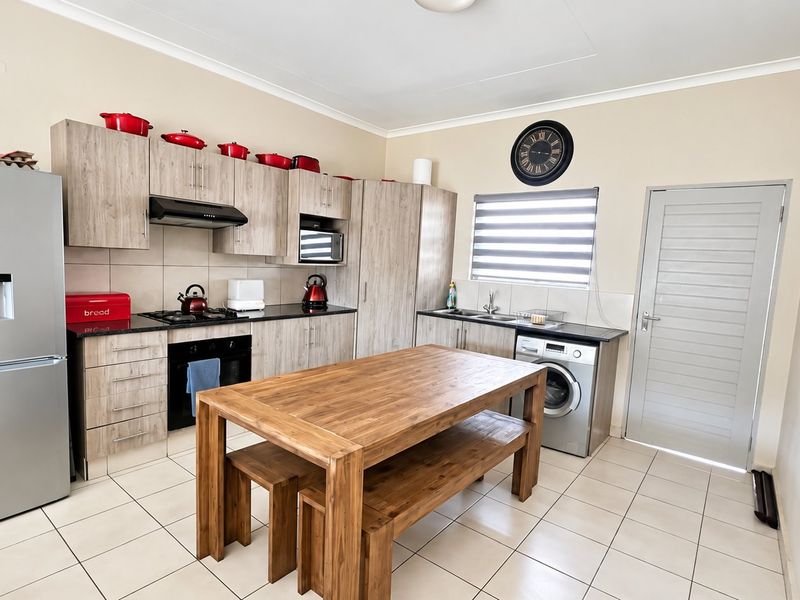 A functional kitchen featuring light wood-finish cabinetry, dark countertops, a gas hob, built-in oven, and tiled flooring with an integrated laundry appliance space.