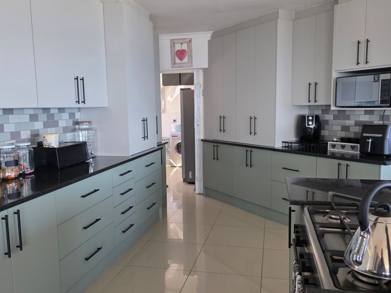Modern kitchen featuring sage green and white cabinetry, black granite countertops, subway tile backsplash, and integrated gas hob with built-in microwave.