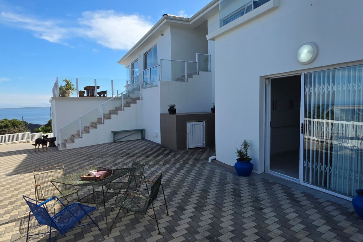 Spacious rear patio area featuring paved flooring, glass balustrades, and an external staircase leading to an upper level with scenic ocean views.