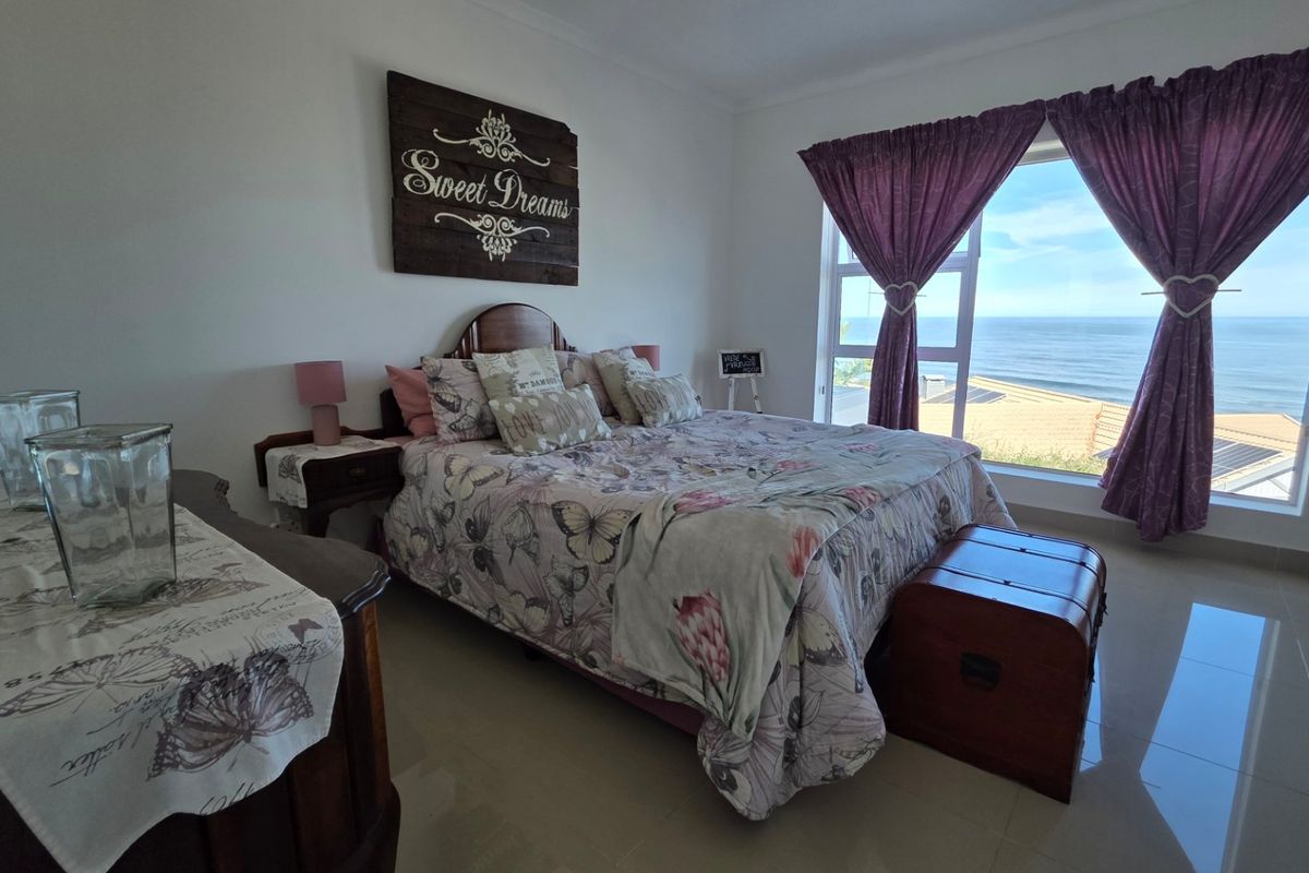 A bright bedroom featuring large windows with expansive ocean views, tiled flooring, and a neutral interior finish.