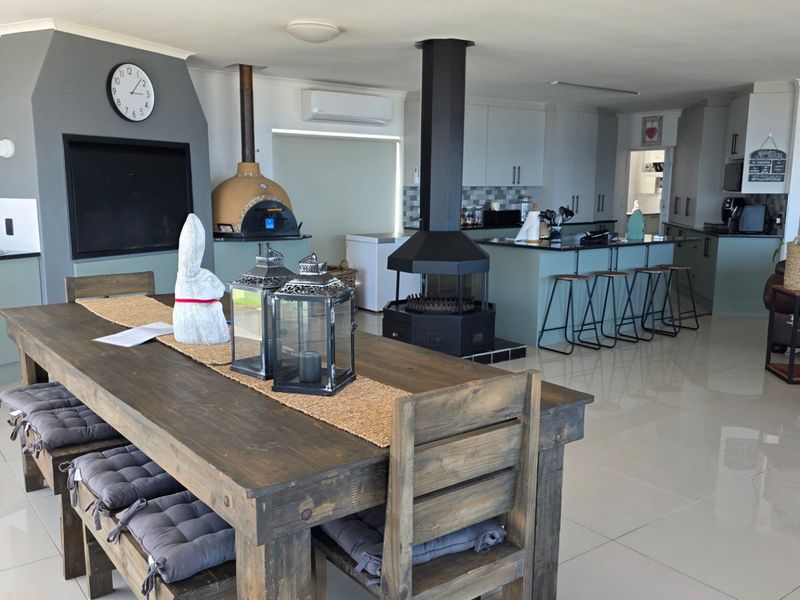 Spacious open-plan living area featuring a modern kitchen with island, central fireplace, built-in braai, and a pizza oven, finished with polished floor tiles.