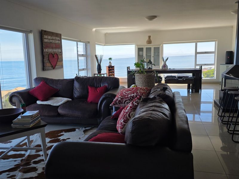 Spacious open-plan living and dining area featuring large sliding glass doors with panoramic ocean views and a built-in fireplace.