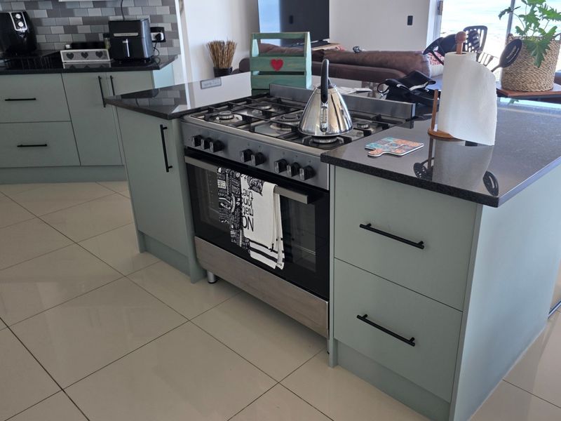 Modern kitchen featuring a central island with a built-in gas stove, oven, granite countertops, and light-colored cabinetry, complemented by sleek tiled flooring.