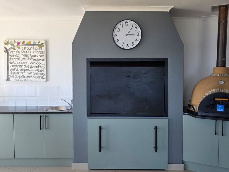 An outdoor entertainment area featuring a built-in braai, a pizza oven, and a functional kitchenette with cabinetry and a sink.
