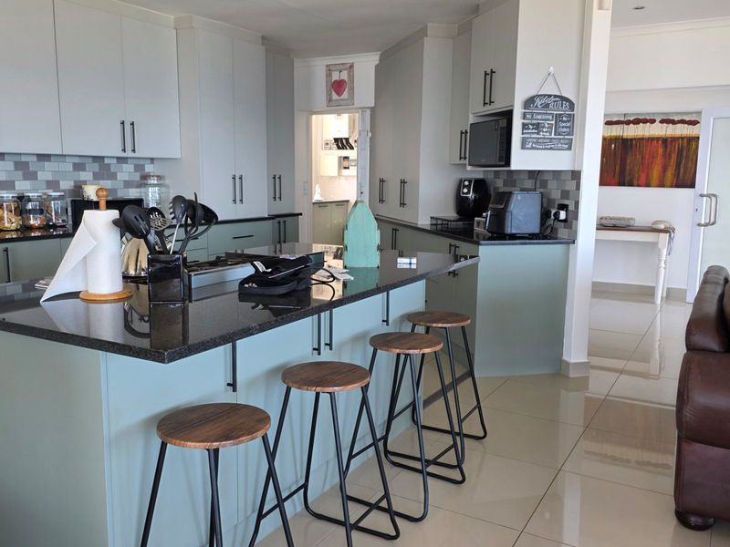 Modern open-plan kitchen featuring a large island with granite countertops, ample cabinetry, and a stylish subway tile backsplash, seamlessly flowing into the living area.