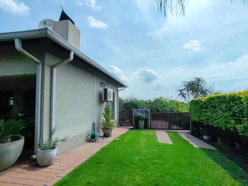 A well-maintained rear garden featuring a paved walkway, established hedging, timber fencing, and a clear view of the property's exterior wall and chimney.