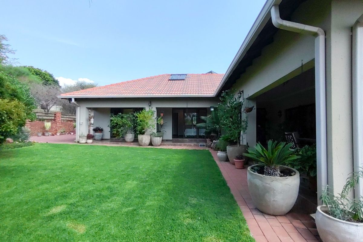 A well-maintained rear exterior view featuring a spacious lawn, brick paved pathways, and a covered patio area with terracotta roof tiles.